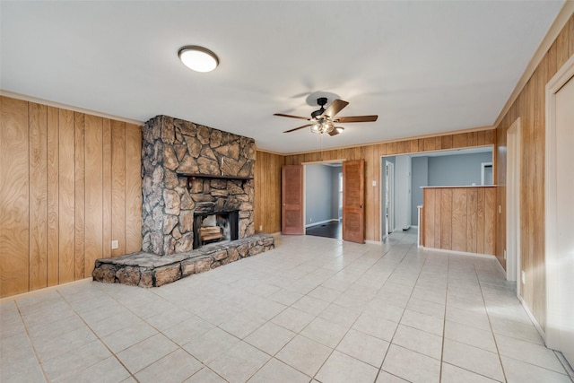 unfurnished living room featuring ceiling fan, wood walls, light tile patterned floors, and a fireplace