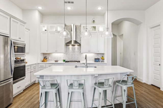 kitchen featuring hardwood / wood-style floors, wall chimney exhaust hood, stainless steel appliances, and an island with sink