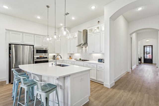 kitchen featuring sink, wall chimney range hood, light hardwood / wood-style flooring, a center island with sink, and appliances with stainless steel finishes