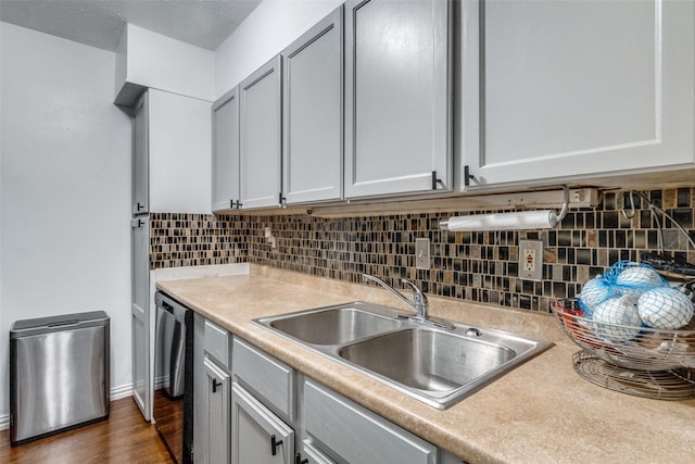 kitchen with gray cabinetry, dark wood-type flooring, sink, stainless steel dishwasher, and tasteful backsplash