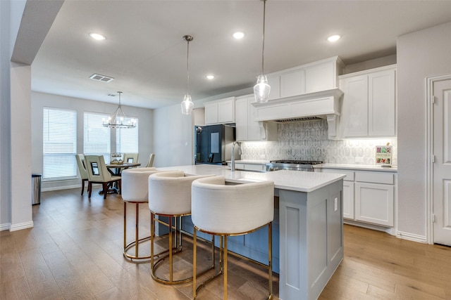 kitchen with a center island with sink, light hardwood / wood-style floors, black fridge, and white cabinets