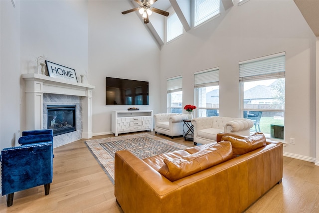 living room featuring light hardwood / wood-style floors, a tile fireplace, ceiling fan, and a high ceiling