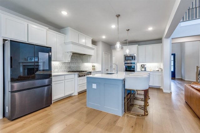 kitchen with sink, stainless steel appliances, pendant lighting, a center island with sink, and white cabinets