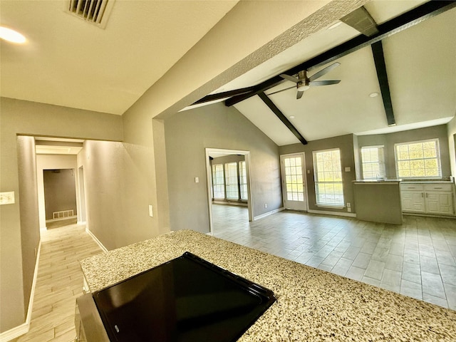 kitchen featuring ceiling fan, vaulted ceiling with beams, and light stone countertops