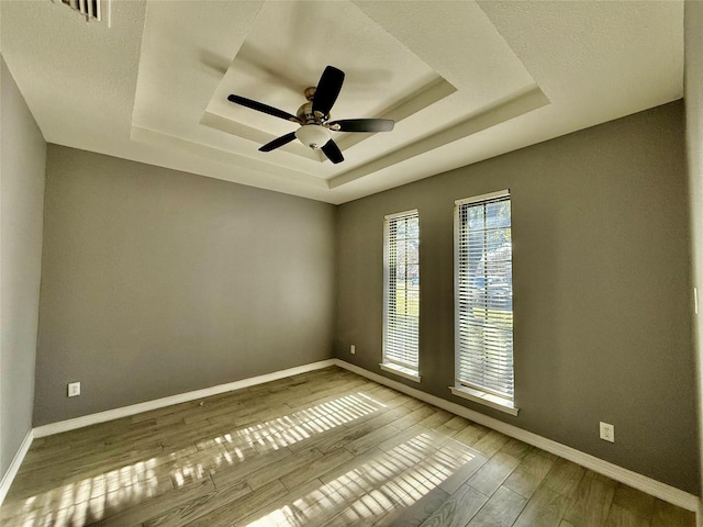 spare room with a raised ceiling, ceiling fan, and wood-type flooring