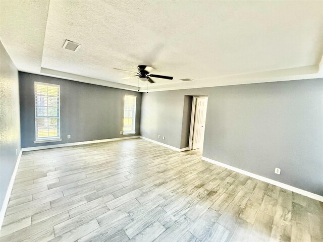 empty room with ceiling fan, a raised ceiling, and a textured ceiling