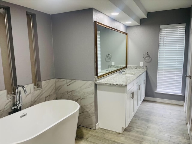 bathroom with tile walls, vanity, a washtub, and hardwood / wood-style floors