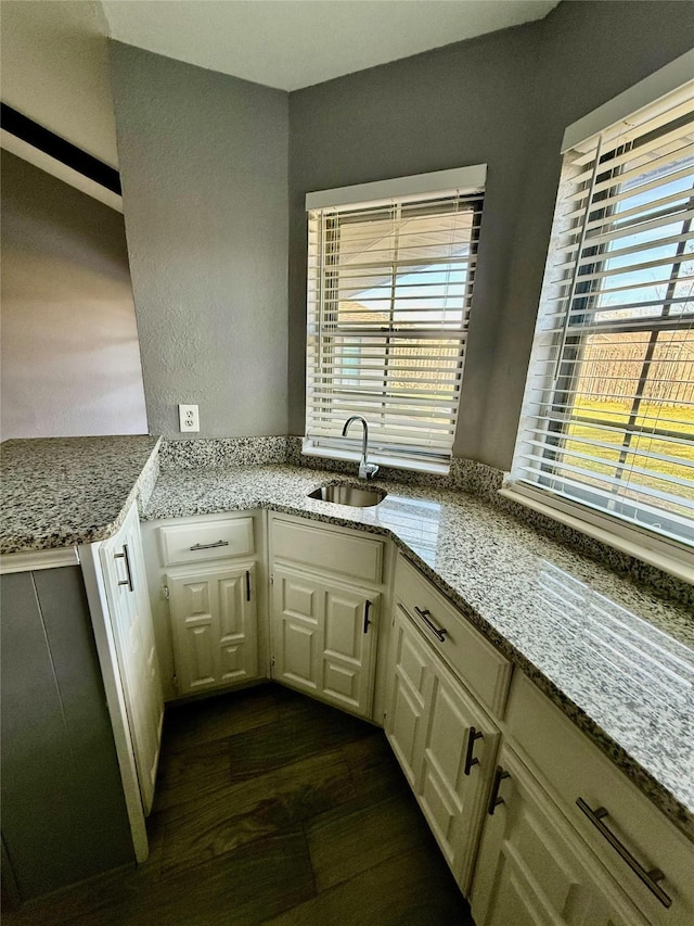 kitchen with light stone countertops, white cabinets, dark hardwood / wood-style flooring, and sink