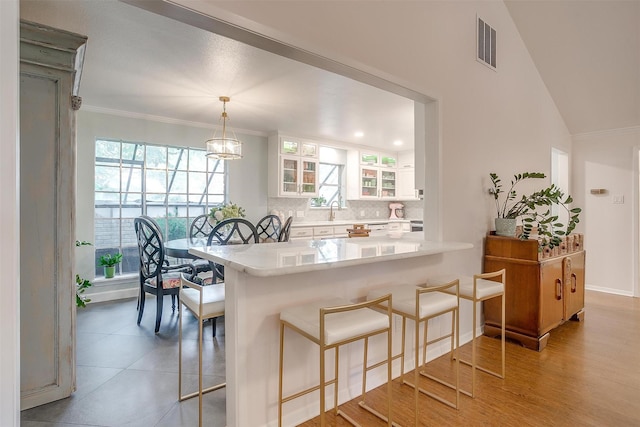 kitchen with a kitchen bar, hanging light fixtures, kitchen peninsula, decorative backsplash, and white cabinets