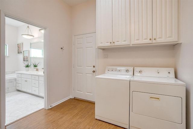 washroom with cabinets, washing machine and clothes dryer, and light hardwood / wood-style flooring