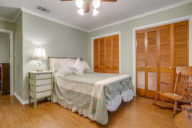 bedroom featuring crown molding, ceiling fan, wood-type flooring, a textured ceiling, and multiple closets