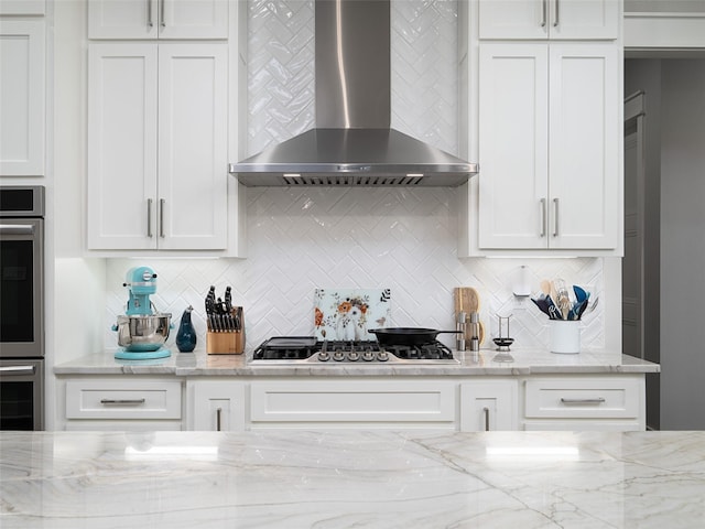 kitchen featuring appliances with stainless steel finishes, tasteful backsplash, white cabinetry, and wall chimney range hood