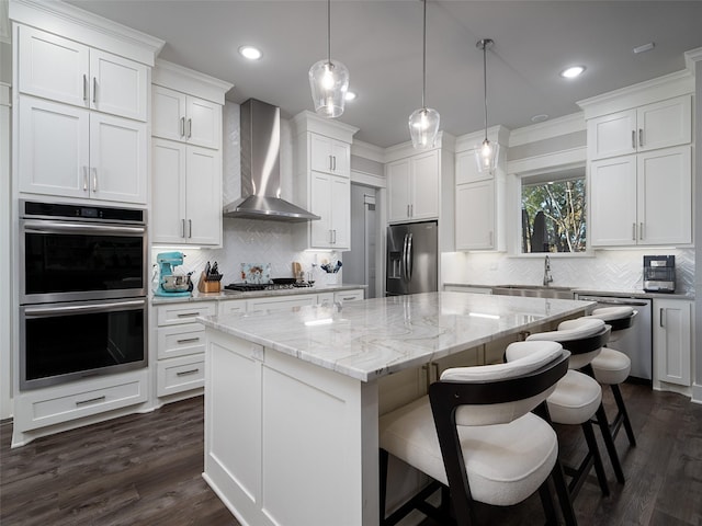 kitchen with decorative backsplash, appliances with stainless steel finishes, wall chimney exhaust hood, a center island, and white cabinetry