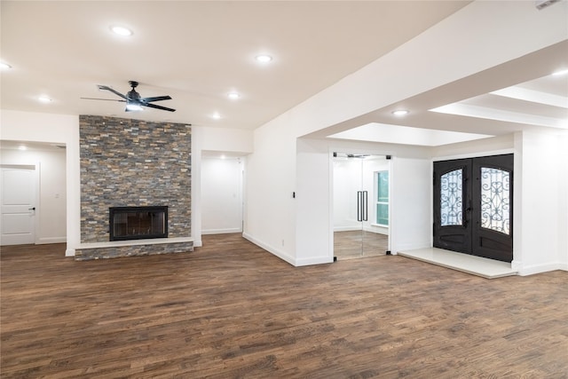 unfurnished living room with french doors, a stone fireplace, ceiling fan, and dark wood-type flooring