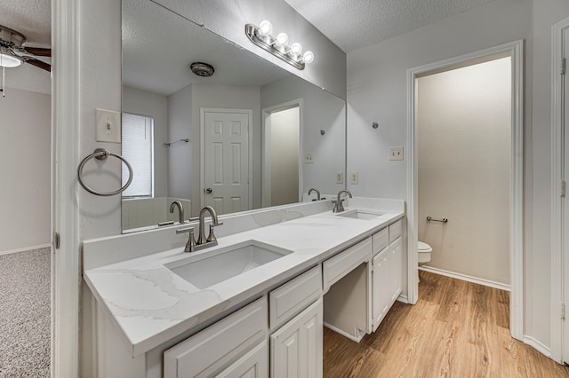 bathroom featuring ceiling fan, a textured ceiling, toilet, vanity, and hardwood / wood-style flooring