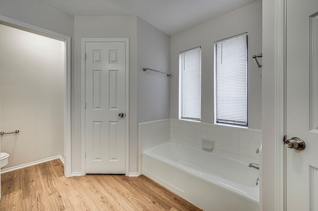 bathroom featuring hardwood / wood-style floors, a textured ceiling, toilet, and a bathing tub