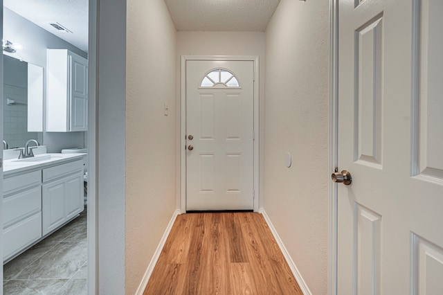 entryway with a textured ceiling, light wood-type flooring, and sink