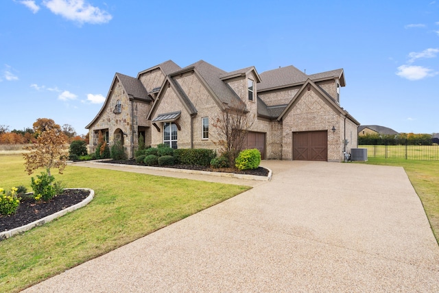 french country inspired facade featuring driveway, roof with shingles, brick siding, central AC unit, and an attached garage