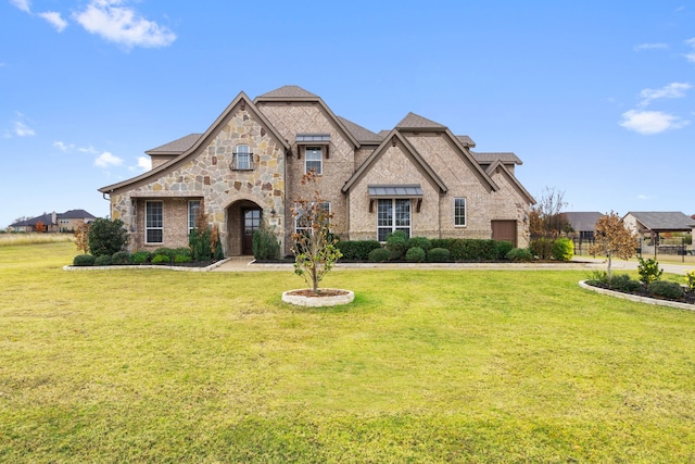french country inspired facade with a front lawn, stone siding, and roof with shingles