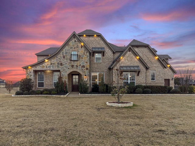 french country style house featuring stone siding, a front yard, brick siding, and roof with shingles