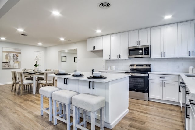 kitchen with stainless steel appliances, white cabinetry, a center island, and a breakfast bar