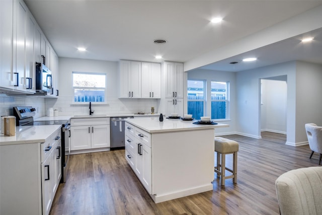 kitchen featuring backsplash, stainless steel appliances, wood-type flooring, white cabinets, and a kitchen island