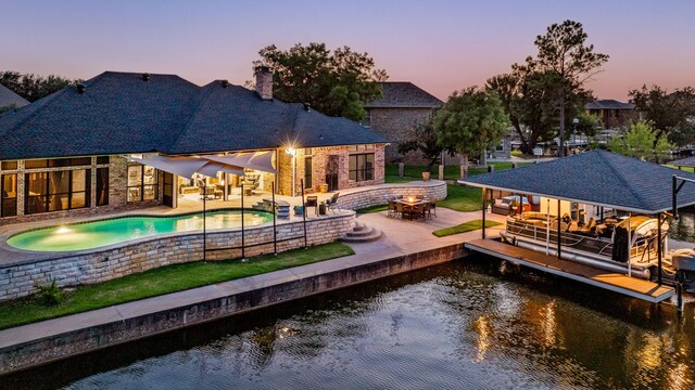 pool at dusk with an in ground hot tub, a patio, a water view, and a dock