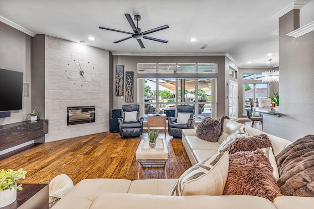 living room featuring a tile fireplace, ceiling fan with notable chandelier, hardwood / wood-style flooring, and crown molding