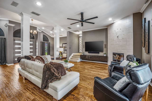 living room featuring a tile fireplace, vaulted ceiling, hardwood / wood-style flooring, ceiling fan with notable chandelier, and ornamental molding