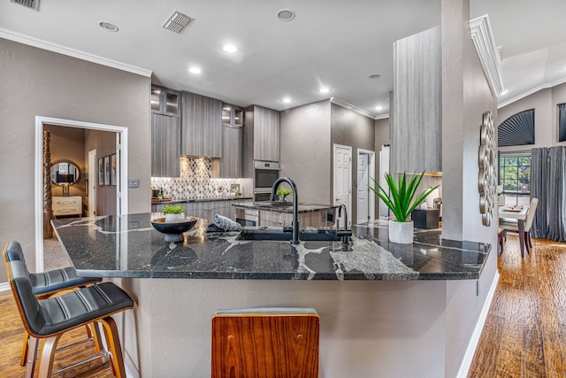 kitchen with kitchen peninsula, a kitchen bar, ornamental molding, sink, and light hardwood / wood-style floors