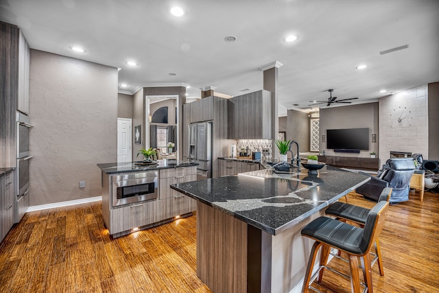 kitchen featuring ornamental molding, ceiling fan, a spacious island, light hardwood / wood-style flooring, and a breakfast bar area