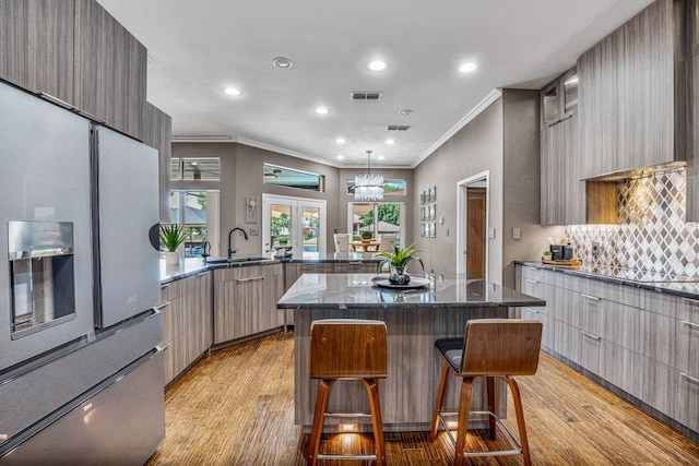 kitchen with a kitchen bar, french doors, light wood-type flooring, ornamental molding, and dark stone countertops