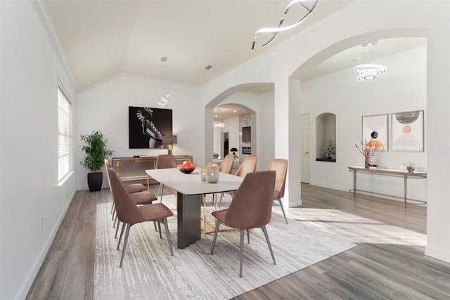 dining space featuring wood finished floors, visible vents, baseboards, arched walkways, and crown molding