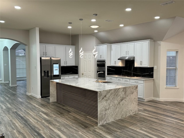 kitchen featuring visible vents, arched walkways, a large island with sink, decorative backsplash, and appliances with stainless steel finishes