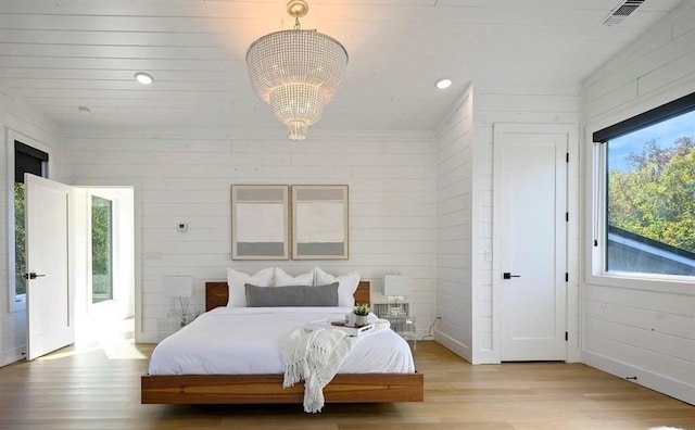 bedroom with light wood-type flooring, an inviting chandelier, and wooden walls