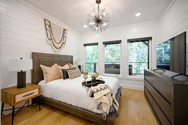 bedroom with light wood-type flooring, an inviting chandelier, and wood walls