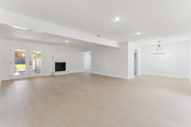 unfurnished living room with french doors, a chandelier, a brick fireplace, and light wood-type flooring