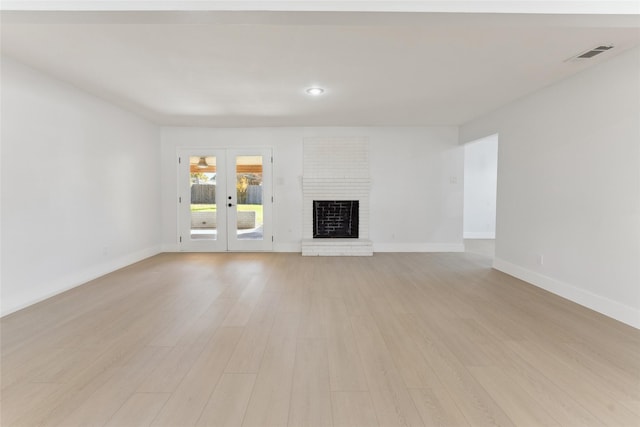 unfurnished living room featuring light wood-type flooring, a fireplace, and french doors