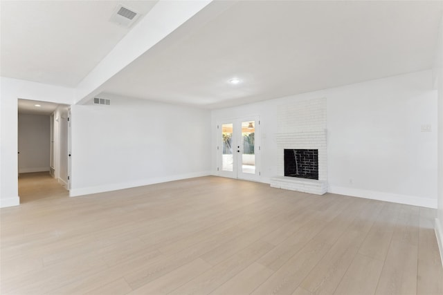 unfurnished living room with a brick fireplace, french doors, and light hardwood / wood-style flooring