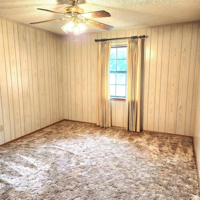 carpeted spare room featuring a textured ceiling, ceiling fan, and wooden walls