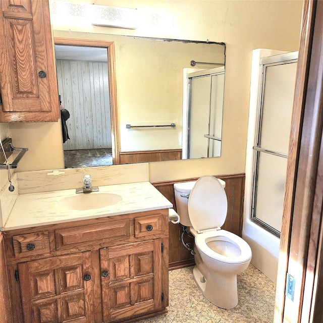 full bathroom featuring wood walls, vanity, enclosed tub / shower combo, and toilet