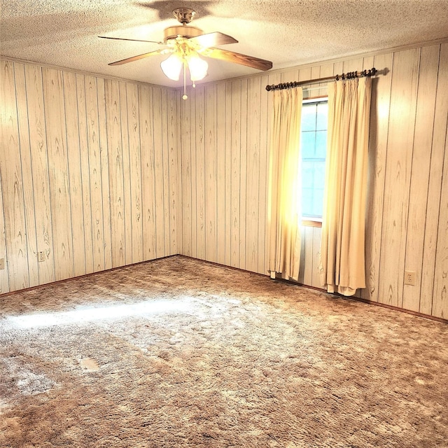 carpeted spare room featuring wood walls, ceiling fan, and a textured ceiling