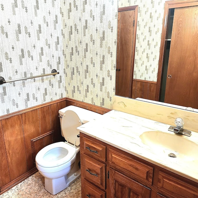 bathroom with vanity, wood walls, and toilet