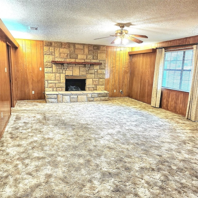 unfurnished living room featuring a textured ceiling, carpet floors, a stone fireplace, and wood walls