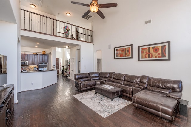 living room with dark hardwood / wood-style floors, ceiling fan, and a towering ceiling