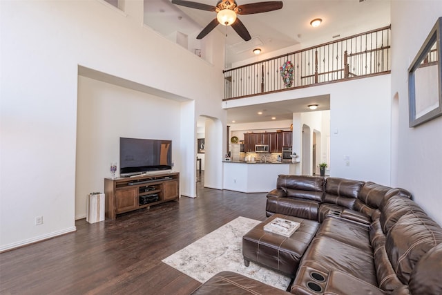 living room with a high ceiling, ceiling fan, and dark wood-type flooring