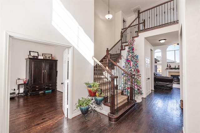 foyer entrance with a tile fireplace, a towering ceiling, and dark wood-type flooring