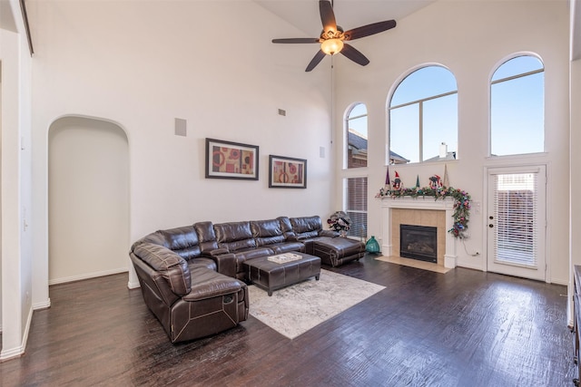 living room featuring a high ceiling, ceiling fan, dark wood-type flooring, and a tiled fireplace