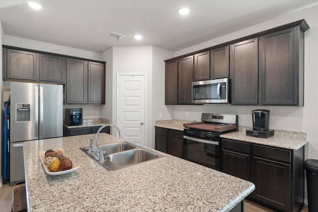 kitchen featuring a center island with sink, stainless steel appliances, visible vents, a sink, and dark brown cabinets