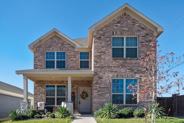 traditional-style home with covered porch, brick siding, and fence